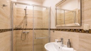 Ein modernes Badezimmer mit einer Duschkabine, einem weißen Waschbecken mit Spiegel und einem Fliesenboden.