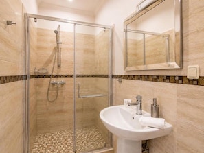A modern bathroom with a glass-enclosed shower, a white sink with a mirror, and a tiled floor. - Standart Double Room (Rīga)