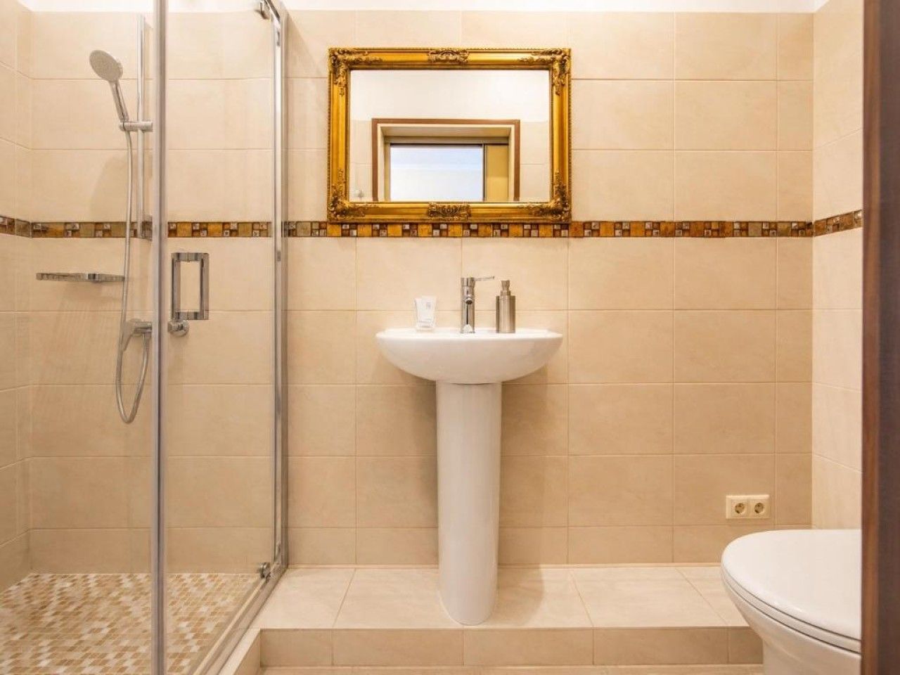 Ein Badezimmer mit Duschkabine aus Glas, einem Standwaschbecken und einer Toilette.