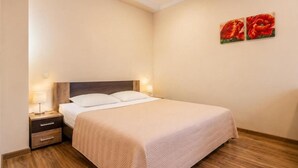 Ein ordentlich bezogenes Bett mit Kopfteil, ein Nachttisch mit Lampe sowie zwei an der Wand hängende Bilder.