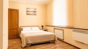 Ein Schlafzimmer mit einem Bett, einem Nachttisch, einem Fenster mit Jalousien und einer Heizung.