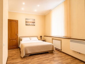 A bedroom with a bed, a nightstand, a window with blinds, and a radiator. - Standart Double Room (Rīga)