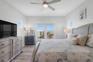 Une chambre à coucher comprenant un lit, une télévision, une commode, une table de chevet et un ventilateur de plafond.