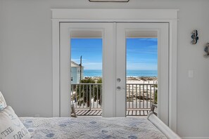 Une chambre avec un lit, une vue sur la plage par une porte et un balcon avec une balustrade.