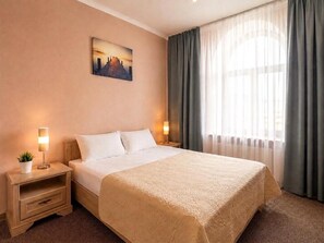 Ein Hotelzimmer mit einem großen Bett, einem Nachttisch mit Lampe, einem Gemälde an der Wand und einem Fenster mit Vorhängen.