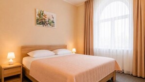 Una habitación de hotel con una cama, dos lámparas de noche, un ventanal con cortinas y un cuadro colgado en la pared.