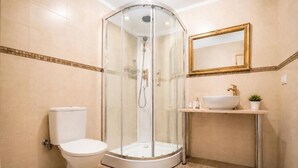 Un baño con ducha envuelta en cristal, inodoro, lavamanos con grifo dorado y espejo con marco dorado.