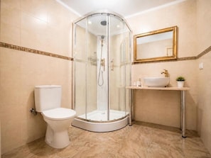 Ein Badezimmer mit einer Duschkabine aus Glas, einer Toilette, einem Waschbecken mit goldfarbenem Wasserhahn und einem Spiegel mit goldener Rahmung.