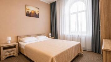 Ein Hotelzimmer mit einem Bett, einem Nachttisch, einer Lampe, einem Bild an der Wand und einem Fenster mit Vorhängen.