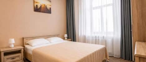 Une chambre d’hôtel avec un lit, une table de chevet, une lampe, un tableau au mur et une fenêtre avec des rideaux.