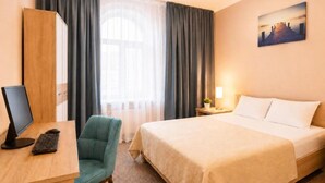 Habitación de hotel con cama, escritorio con computadora, silla, ventana con cortinas e imagen colgada en la pared.