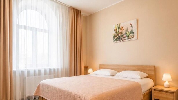 Habitación de hotel con cama, dos lámparas de noche, una ventana con cortinas y un cuadro colgado en la pared.