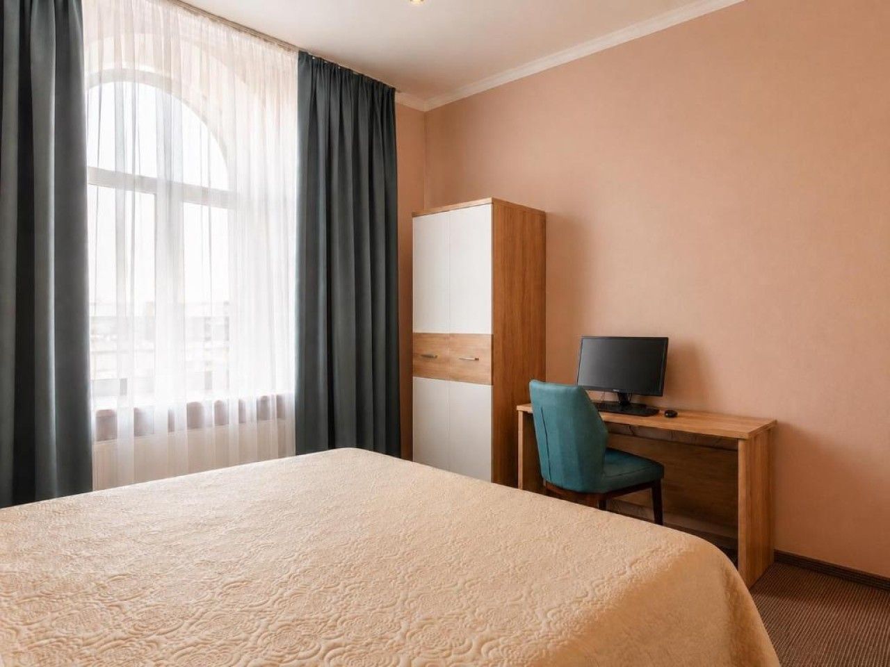 A hotel room with a bed, a desk with a computer, and a wardrobe.