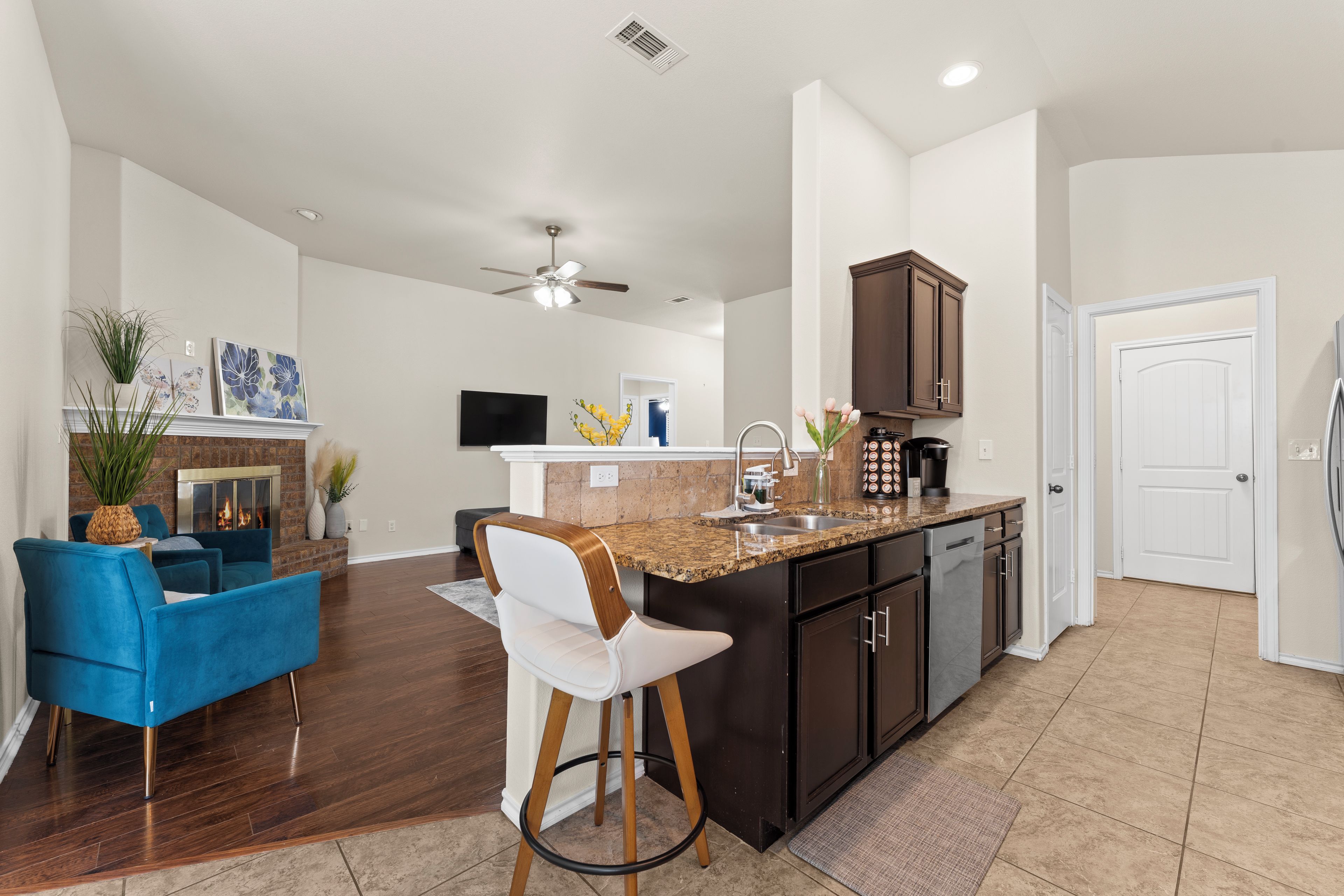 A modern kitchen with a bar area, wooden flooring, and a ceiling fan.