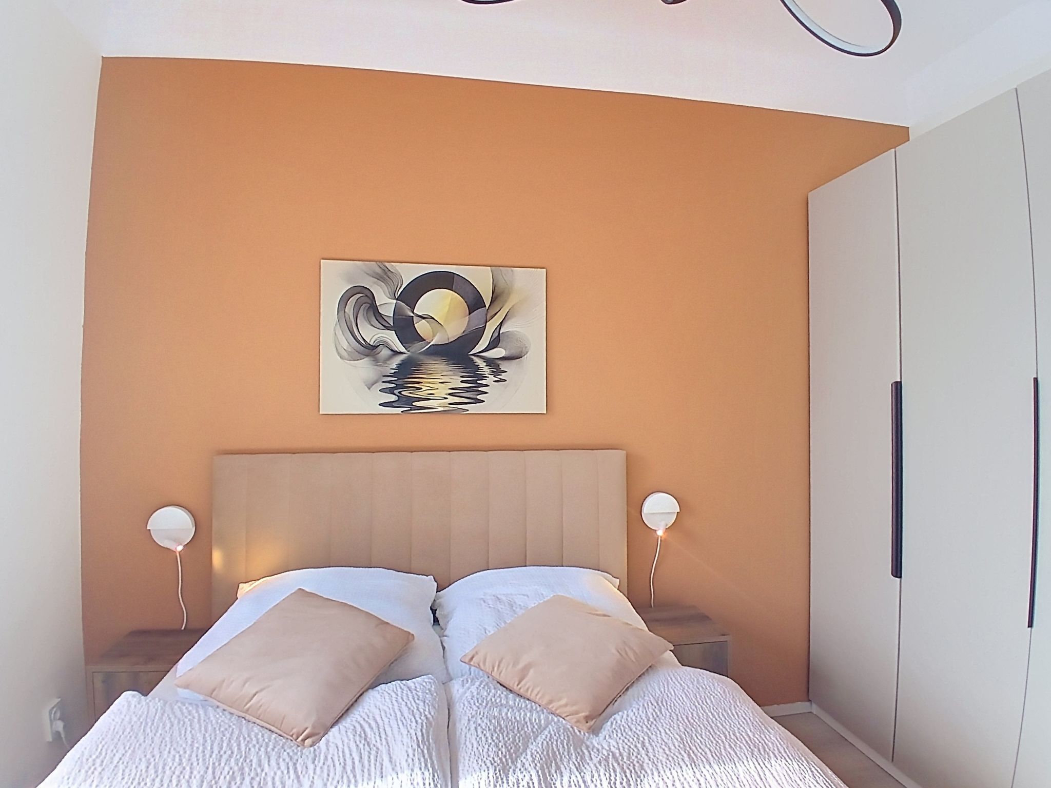 A bedroom with a bed, two bedside lamps, a wall-mounted artwork, and a wardrobe.