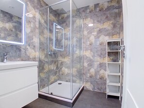 Ein modernes Badezimmer mit einer Duschkabine aus Glas, einem weißen Waschtisch und einer Wand mit Marmoroptik.