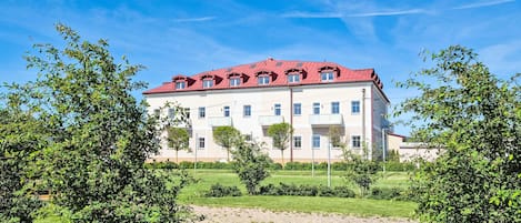 A multi-story building with a red roof, surrounded by greenery and a clear sky.