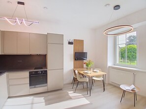 Eine moderne Küche mit integrierten Geräten, ein Essbereich mit Holztisch und Stühlen sowie ein großes Fenster mit Blick auf Grünflächen.