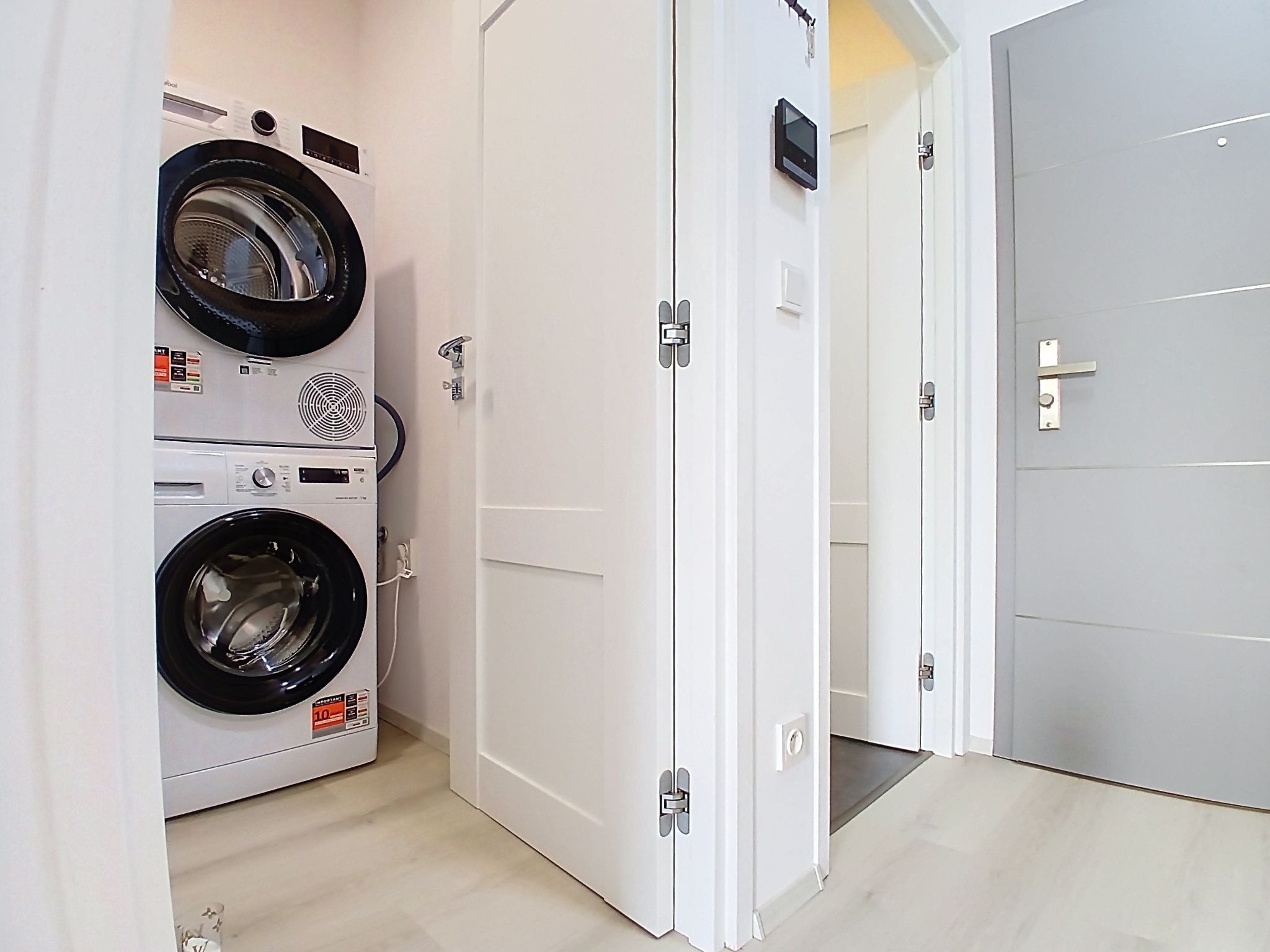 A laundry room with two stacked washing machines, white doors, and a tiled floor.