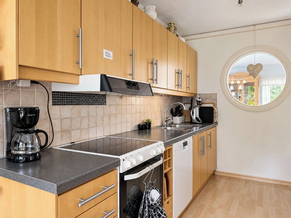 Una cocina moderna con armarios de madera, horno empotrado, cafetera y un espejo redondo con detalle de corazón.