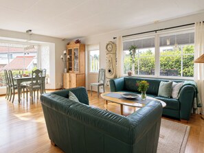 A living room with a green sofa, wooden dining table, and a large window with a view of greenery. - Cityhuset by Interhome (Falkenberg)