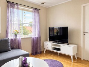 Una sala de estar moderna con un televisor de pantalla plana sobre un mueble blanco, un sofá gris y una mesa de centro redonda con objetos decorativos.