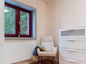Una habitación con ventana, un radiador, una silla blanca y un aparador blanco.
