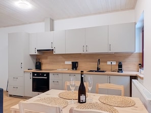Una cocina moderna con armarios blancos, encimera de madera y una mesa de comedor con individuales tejidos y copas de vino.