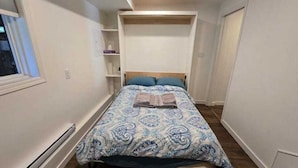 A bedroom with a bed, a built-in shelf, and a window. - Private Studio/bachelor suite (Victoria)