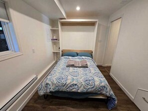 A bedroom with a bed, a built-in shelf, and a window. - Private Studio/bachelor suite (Victoria)