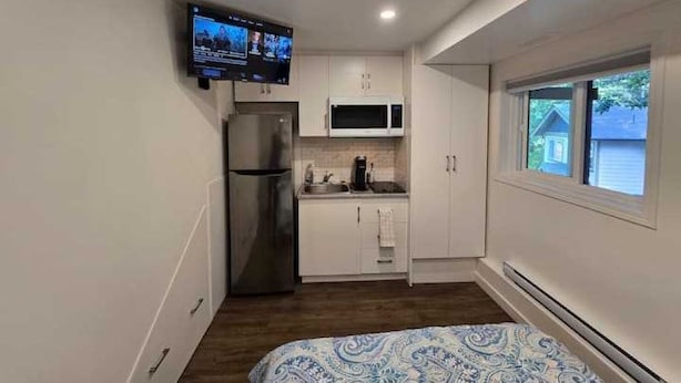 A compact room with a kitchenette, a bed, and a television mounted on the wall. - Private Studio/bachelor suite (Victoria)