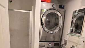A compact laundry room with two stacked front-loading washing machines, a small sink, and a toilet. - Private Studio/bachelor suite (Victoria)