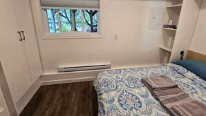 A bedroom with a bed, a window with blinds, a heater, and a wardrobe. - Private Studio/bachelor suite (Victoria)