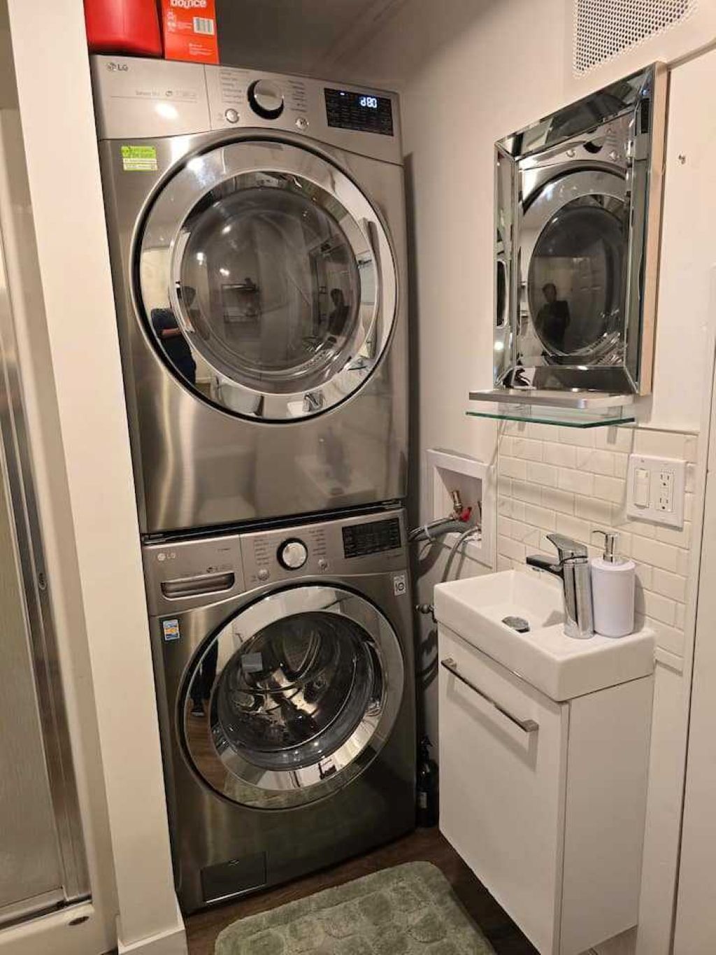 A compact laundry room with two stacked front-loading washing machines and a small sink with a mirror above it.