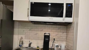 A kitchen with white cabinets, a microwave, a coffee maker, and a sink. - Private Studio/bachelor suite (Victoria)