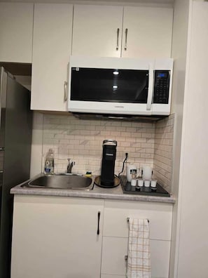 A kitchen with white cabinets, a microwave, a coffee maker, and a sink. - Private Studio/bachelor suite (Victoria)