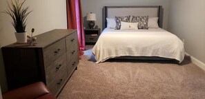 Ein Schlafzimmer mit einem Bett, einem Schminktisch, einem Nachttisch, einer Lampe und einer Topfpflanze.