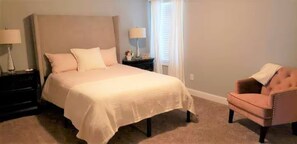 Quarto com cama, mesas de cabeceira, uma cadeira e uma janela com cortinas.