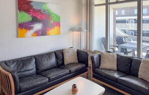 Ein modernes Wohnzimmer mit einem schwarzen Ledersofa, einem weißen Couchtisch und einem farbenfrohen, abstrakten Gemälde an der Wand.
