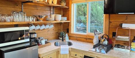 A wooden cabin kitchen with a refrigerator, microwave, stove, sink, and wooden cabinets.