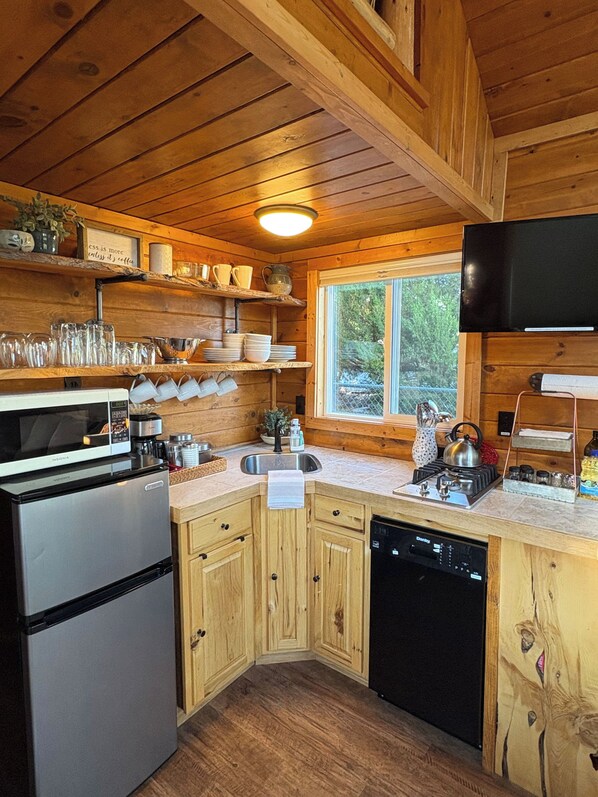 A wooden cabin kitchen with a refrigerator, microwave, stove, sink, and wooden cabinets.