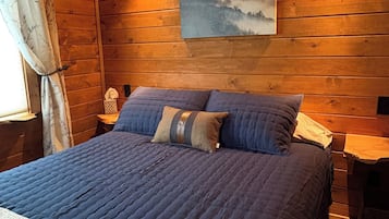 Une pièce aux murs lambrissés, avec un lit, un tableau accroché au mur et une table de chevet.