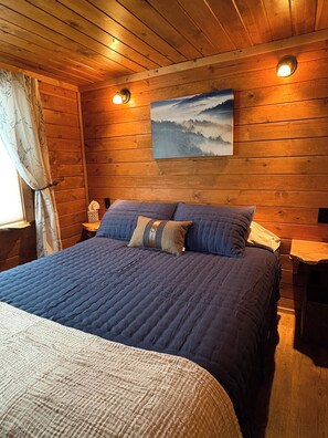 A wooden-paneled room with a bed, a painting on the wall, and a nightstand.