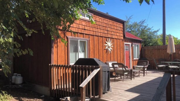 A wooden deck with outdoor furniture, a barbecue grill, and a fenced area. - Little Strawberry Suites, Tiny Home Downtown Prairie City (Prairie City)