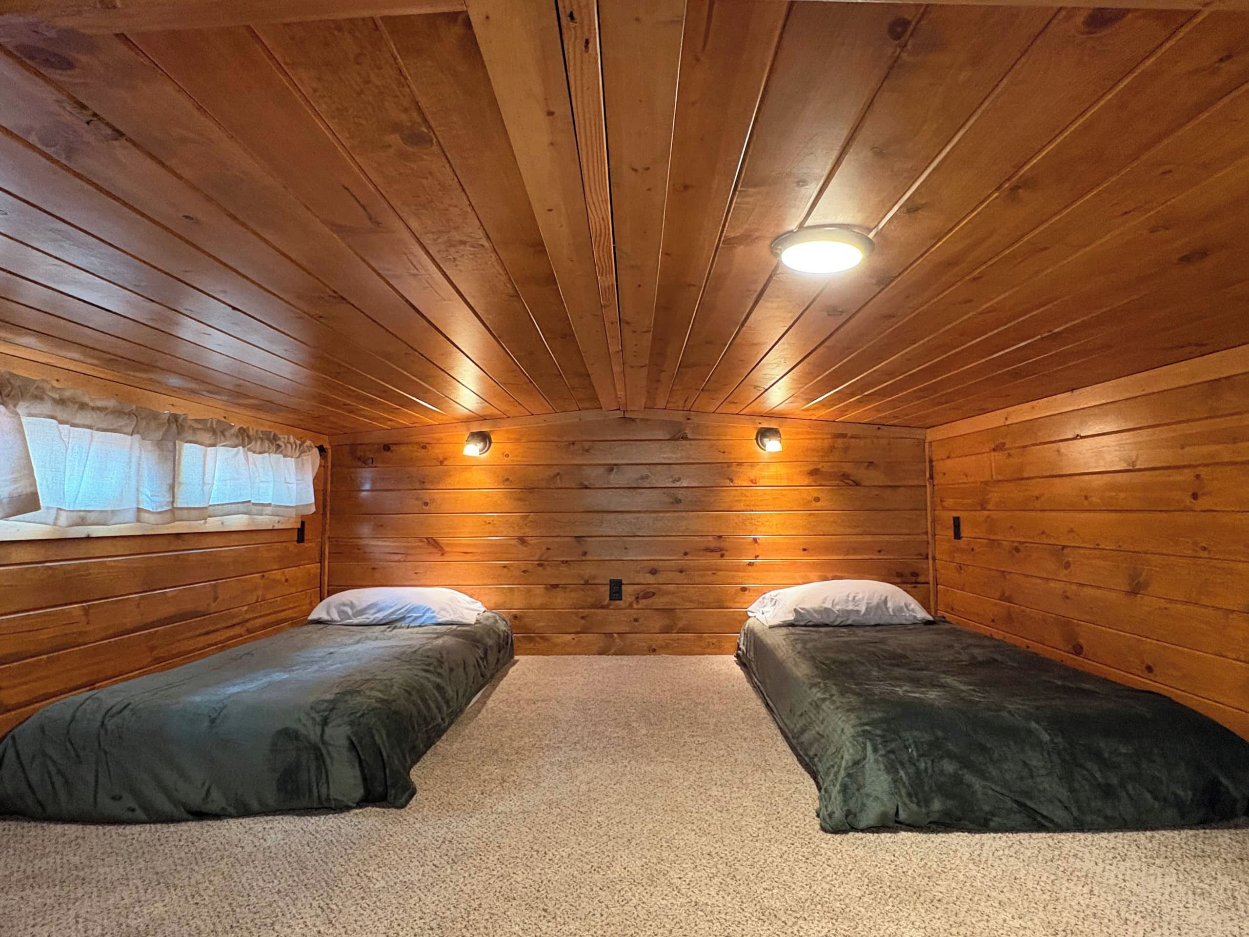 Eine Holzhütte mit zwei Einzelbetten, Holzwänden und einer schrägen Decke mit einer zentralen Leuchte.