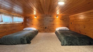 A cabin with two single beds, wooden walls, and a sloped ceiling with a central light fixture. - Little Strawberry Suites, Tiny Home Downtown Prairie City (Prairie City)