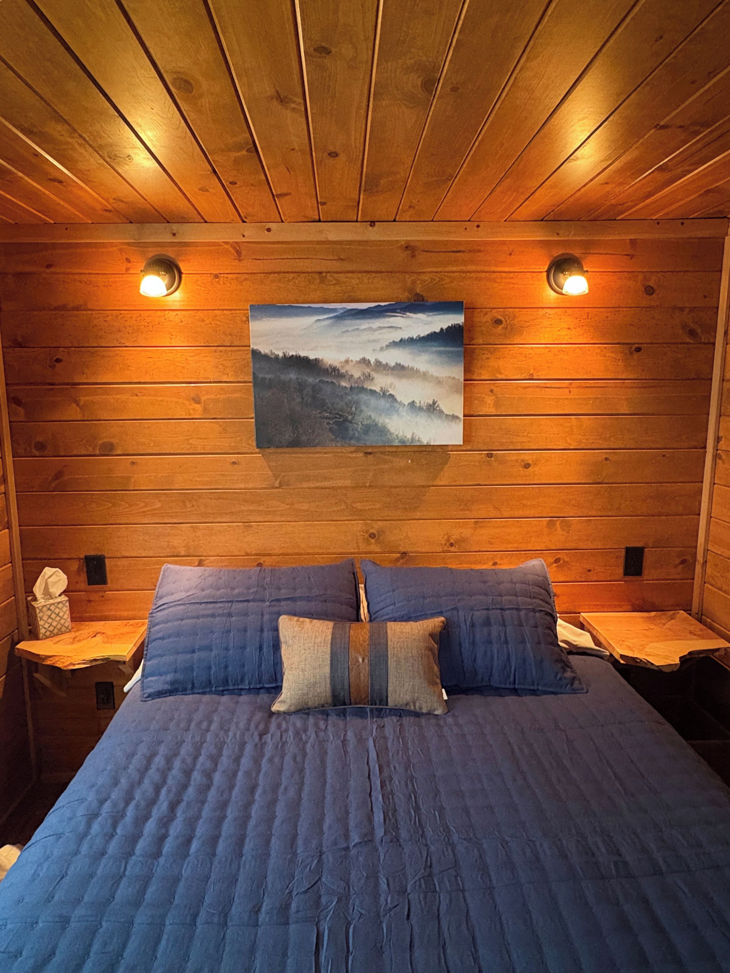A wooden cabin room with a bed, two nightstands, and a wall-mounted picture.