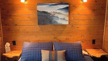 A wooden cabin room with a bed, two nightstands, and a wall-mounted picture.