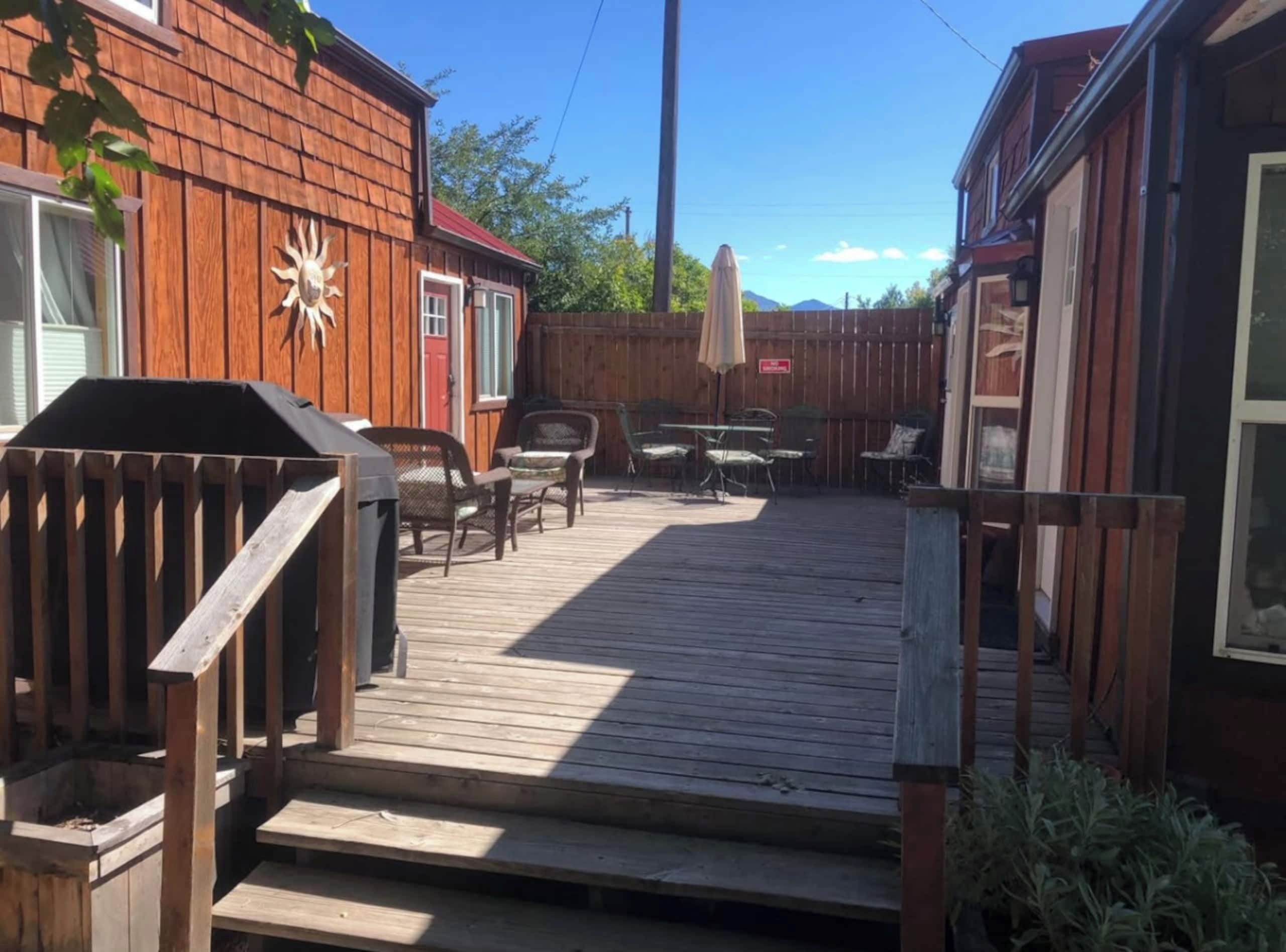 Une terrasse en bois avec des meubles d’extérieur, un barbecue et une cour arrière clôturée.