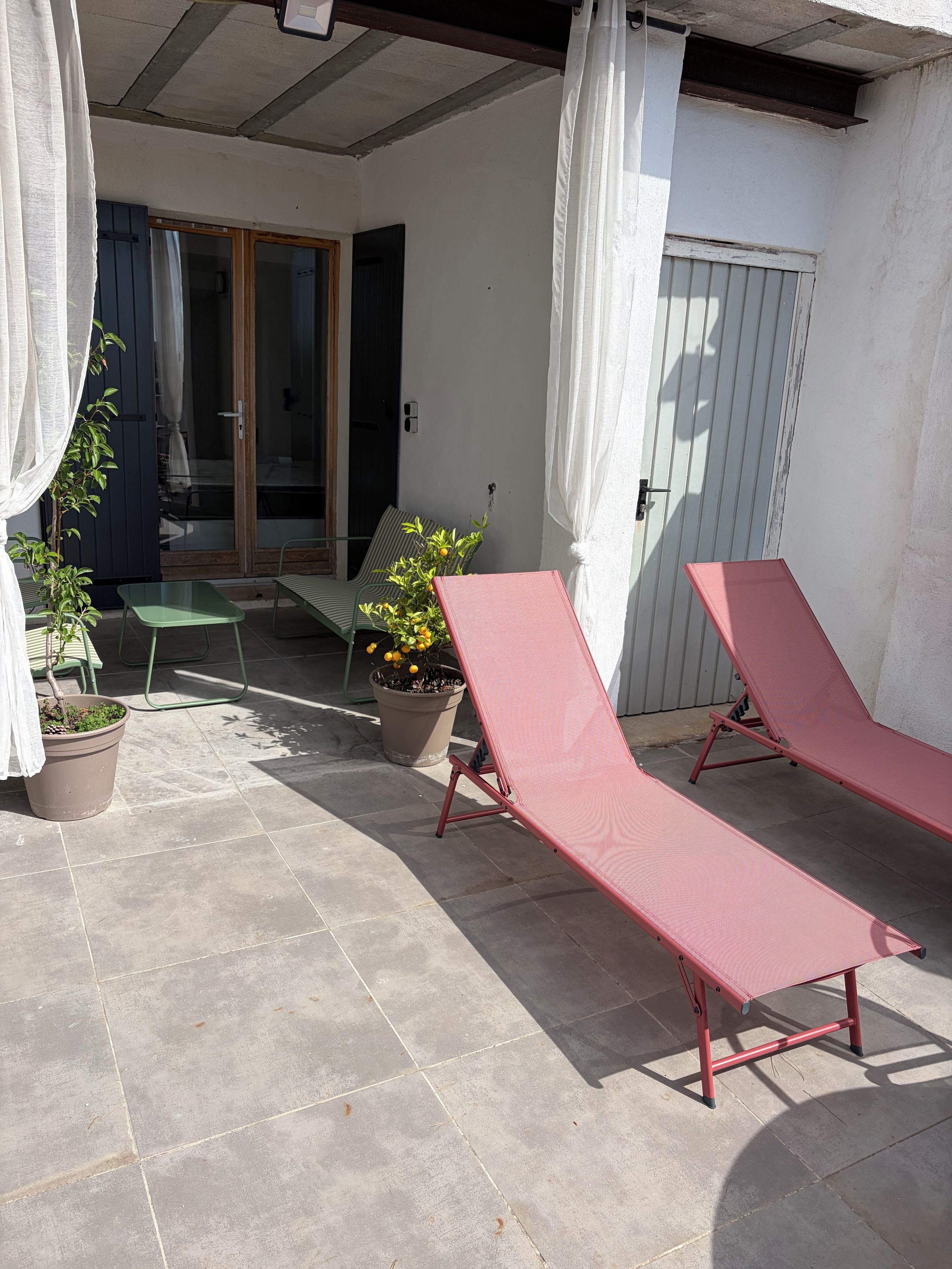 Una veranda riparata con due poltrone rosse, una sedia verde e piante in vaso.